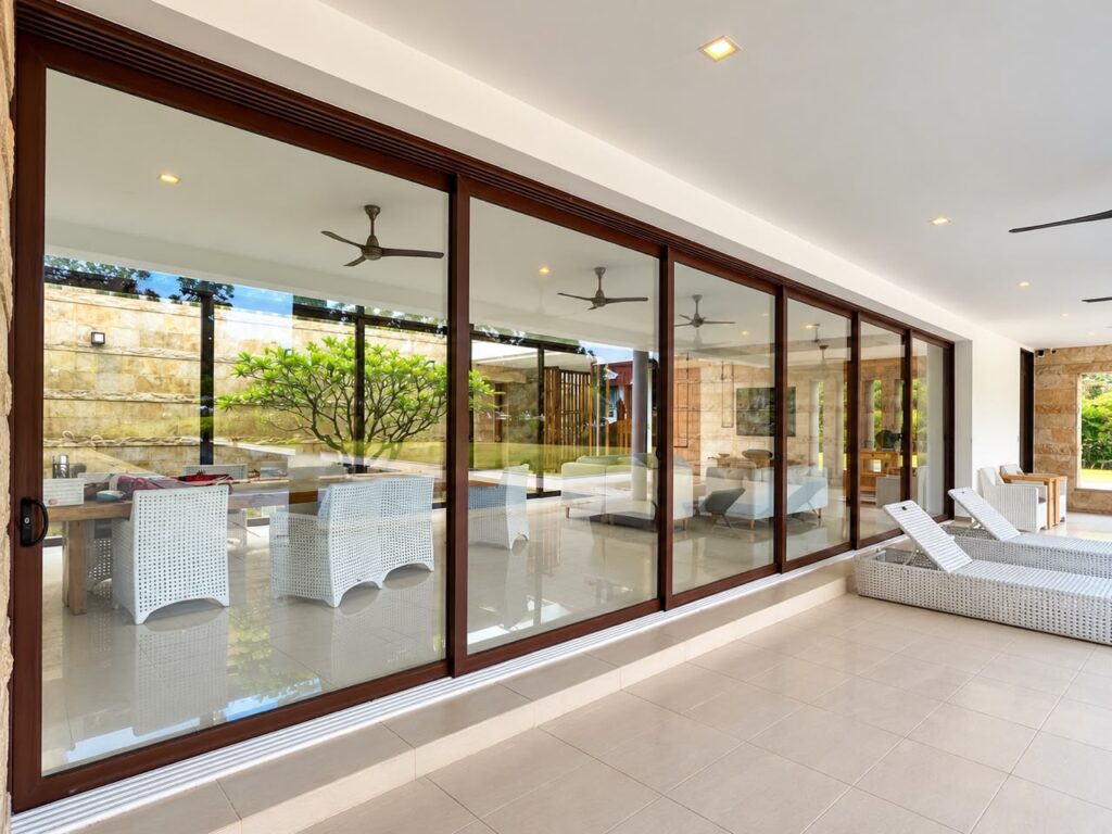 Large-scale aluminium sliding door overlooking a landscaped courtyard, featuring a 10,400mm wide six-panel glass door system by CT Aluminium.
